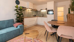 A modern kitchen with a built-in oven, a dining table with chairs, a sofa, and a coffee table. - Apartment in Ostend near the Beach (OSTEND)