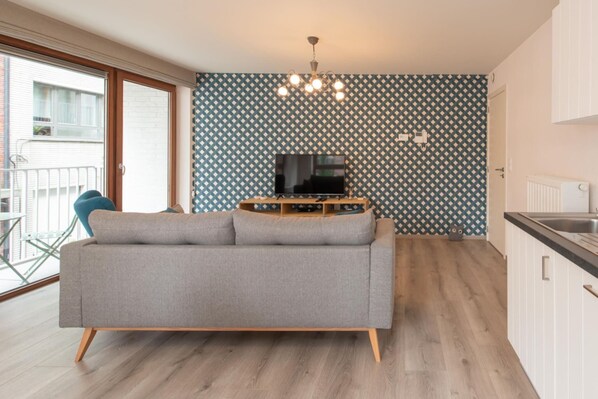 Un salon moderne avec un canapé gris, un téléviseur posé sur un meuble et un mur orné d’un motif.