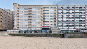 A multi-story hotel with balconies, a beach in the foreground, and a clear sky.