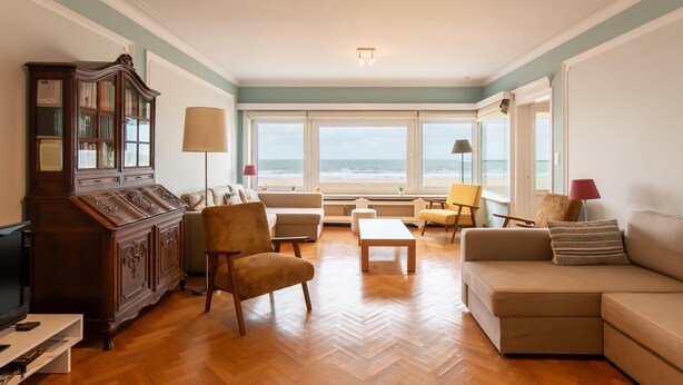 A living room with a wooden herringbone floor, a large cabinet, a sofa, a chair, and a table.