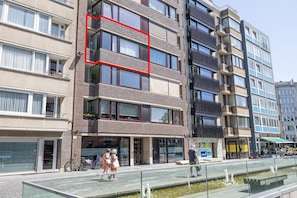 Un immeuble à plusieurs étages doté de balcons, d’une promenade piétonne et d’un élément décoratif aquatique.