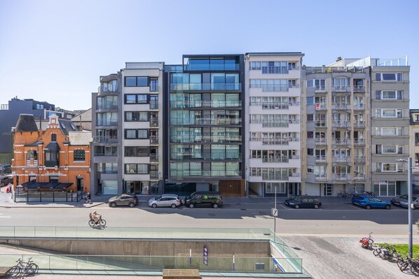 Ein mehrstöckiges Gebäude mit moderner Glasfassade, Balkonen und einem Parkplatz für Autos und Fahrräder.