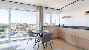A modern kitchen with a large window, a round table, and grey chairs. - Apartment in Ostend near Marina & Park (OSTEND)