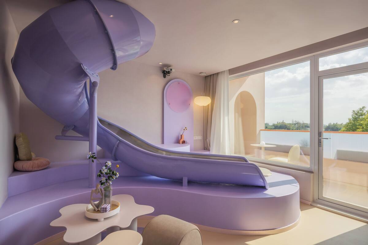 A modern interior with a curved purple slide, a seating area, and large windows offering a view of the outdoors.