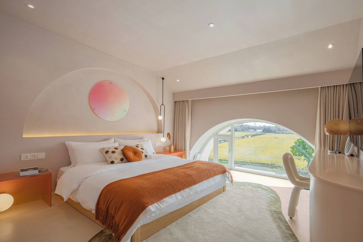 A modern bedroom with a large bed, a view of the outdoors, and a desk with a chair.