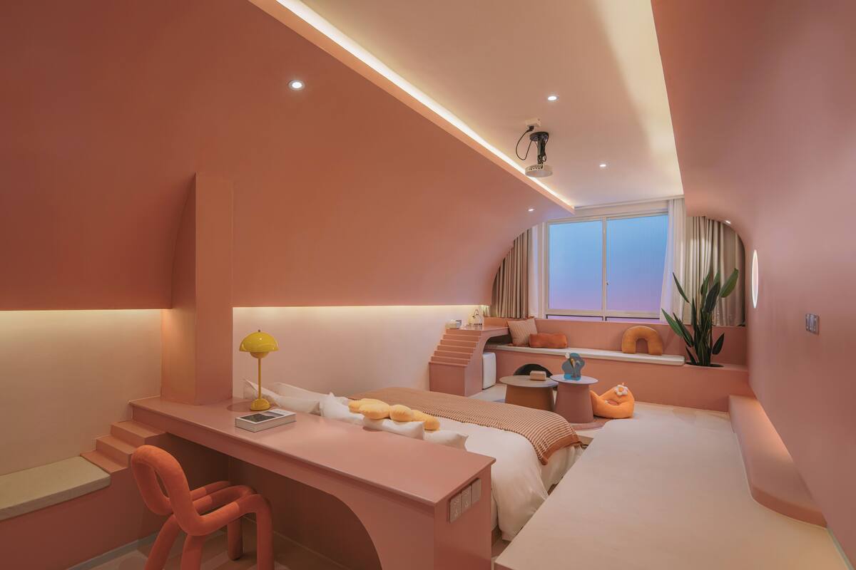 A modern bedroom with a pink color scheme, a desk, a bed, and a window with curtains.