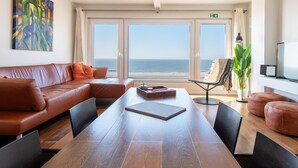 Een moderne woonkamer met een leren bank, een houten eettafel en uitzicht op de oceaan door grote ramen.