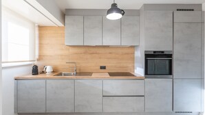A modern kitchen with grey cabinets, a wooden countertop, a built-in oven, and a pendant light. - Modern flat near the sea (Middelkerke)