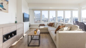 A modern living room with a large window, a sofa, a coffee table, and a TV. - Modern flat near the sea (Middelkerke)