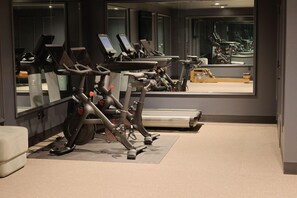 Une salle de sport équipée de nombreux appareils d’exercice, notamment des tapis de course et des vélos d’appartement, disposés en rangée.