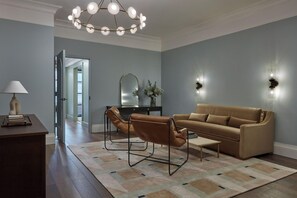 Una sala de estar moderna con un sofá, un sillón y una mesita de centro. Hay una lámpara en una mesita auxiliar, un espejo en la pared y una araña.