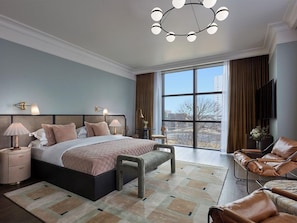 Een moderne slaapkamer met een groot bed, nachtkastjes, een bankje, een sofa en een groot raam met uitzicht op de stad.