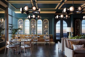 A restaurant interior with high ceilings, arched windows, and a central seating area with tables and chairs.