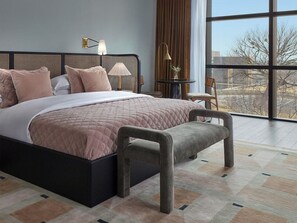 Un dormitorio moderno con una cama grande, dos lámparas de noche, una mesita pequeña y vistas al exterior a través de un ventanal.