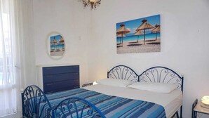 Un dormitorio con una cama, un aparador, una mesita de noche y dos cuadros en la pared que muestran escenas de playa.