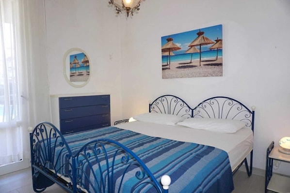 Un dormitorio con una cama, un aparador, una mesita de noche y dos cuadros en la pared que muestran escenas de playa.