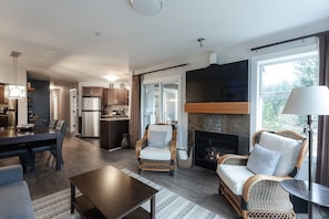 A modern living room with a fireplace, dining area, kitchen, and a large window.