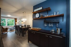 Una cocina moderna con armarios oscuros, un comedor con mesa y sillas, y un ventanal con vistas a zonas verdes.
