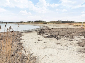 Een zandstrand met een waterpartij, droog gras en een heuvel in de verte.