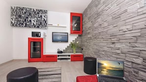 A modern living room with a stone wall, a red entertainment unit, a flat-screen TV, and a laptop on a red ottoman. - Amazing home in Split with private swimming pool, can be inside or outside (Split)