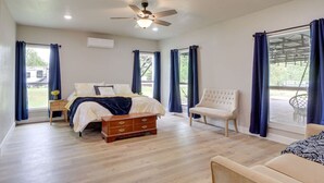 Une chambre spacieuse avec un grand lit, une commode en bois, une chaise et un ventilateur de plafond.