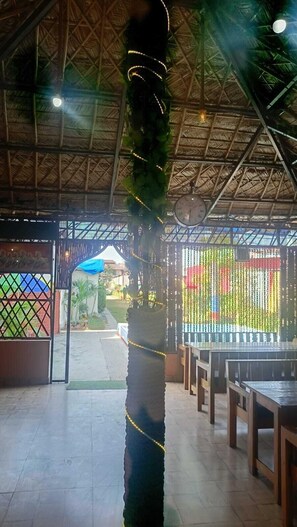 A covered outdoor area with a thatched roof, a decorative hanging element, and a view of the outside. - Krishna Raja Ji Downtown By GRB (Ganga Bhogpur Talla)