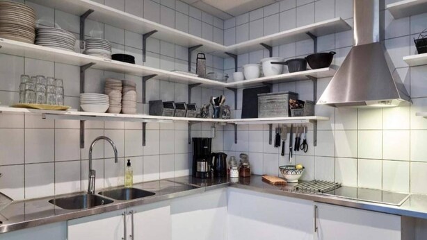 A modern kitchen with white cabinets, stainless steel countertops, and a variety of kitchenware on shelves.