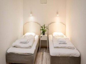 Een kamer met twee eenpersoonsbedden, elk met hoofdbord, nachtkastje met een plant en wandlampen.