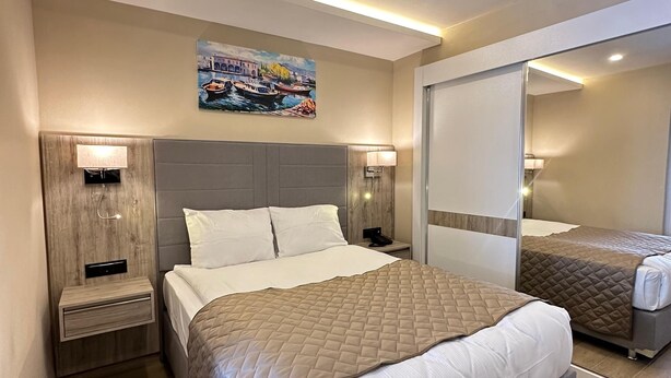 Un dormitorio moderno con una cama grande, mesitas de noche, una lámpara de pared, una luz de techo y un cuadro de barcos.