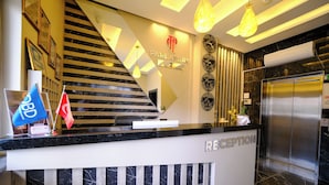 Zona de recepción de un hotel con escalera, mostrador de recepción y ascensor.