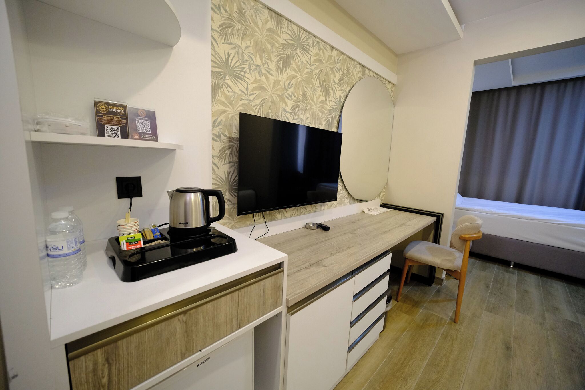 Habitación de hotel con televisión de pantalla plana, cafetera, botella de agua, una silla y una cama.