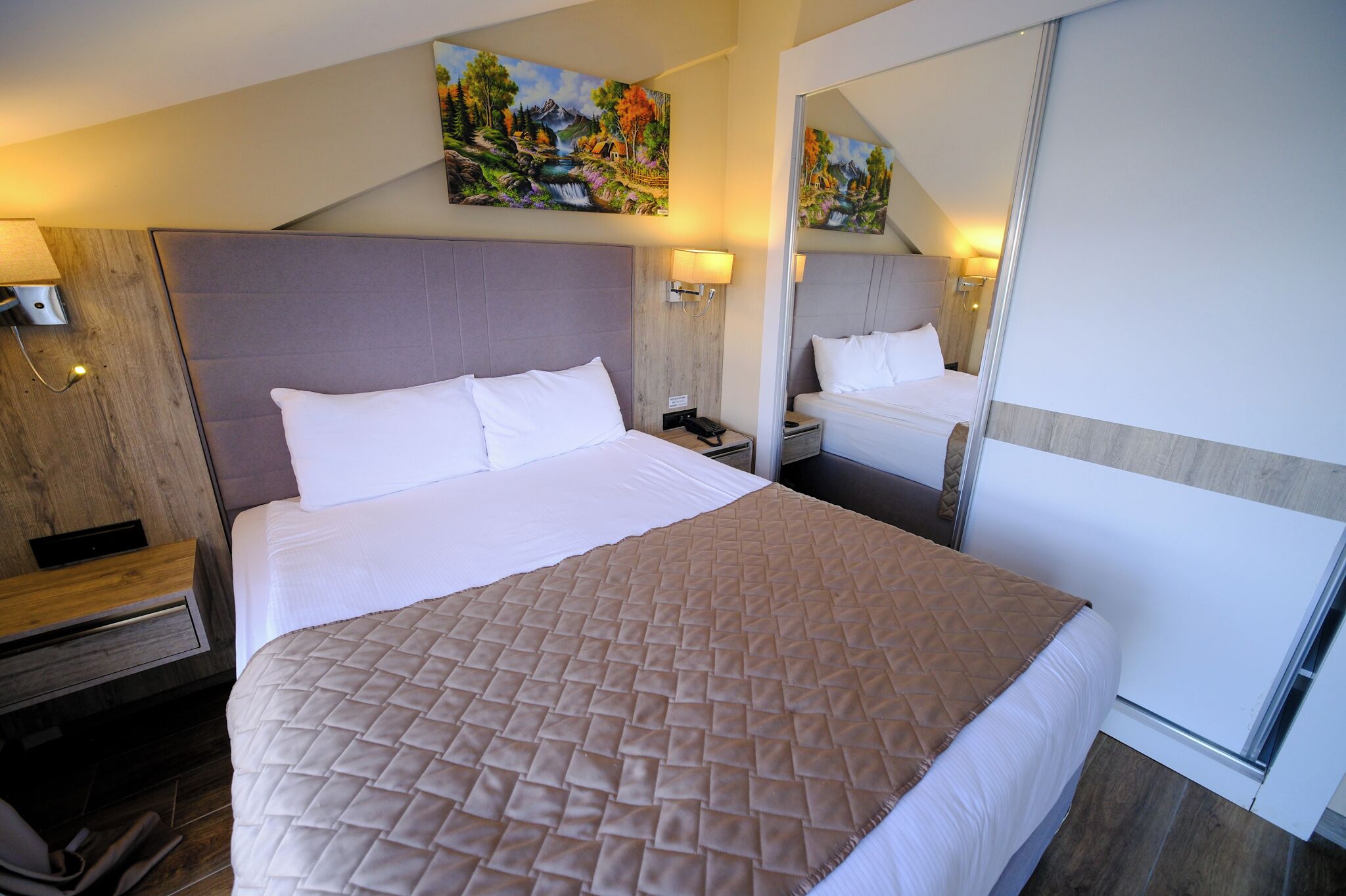 A hotel room with a large bed, a wooden headboard, a nightstand, a mirror, and a painting on the wall.