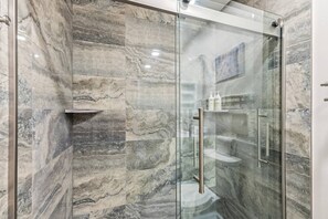 A modern bathroom with a glass-enclosed shower, marble walls, and a built-in shelf with toiletries. - Ski in, Ski Out at The Seasons @ Avon (Avon)