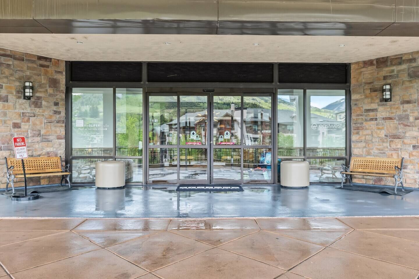 L’entrée d’un hôtel avec des murs en pierre, de grandes portes vitrées et un sol mouillé.