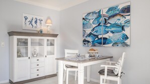 A dining area with a white table, two white chairs, a cabinet with glass doors, and a large fish-themed painting on the wall. - Düneneck 21 - lovingly designed one-room domicile (Zempin)