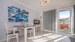 A modern dining area with a white table and chairs, a large fish-themed painting, and a view through a glass door to the outside. - Düneneck 21 - lovingly designed one-room domicile (Zempin)