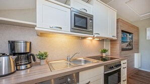 Une cuisine moderne avec des armoires blanches, un four à micro-ondes en acier inoxydable, une machine à café et un évier à deux bacs.