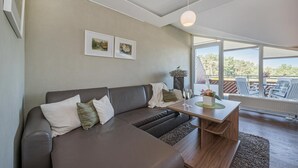 Un salon moderne avec un canapé d’angle, une table basse en bois et une grande fenêtre donnant sur l’extérieur.