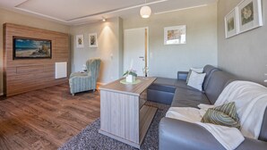 Un salon moderne avec un plancher en bois, un canapé gris, une table basse en bois et un téléviseur fixé au mur.