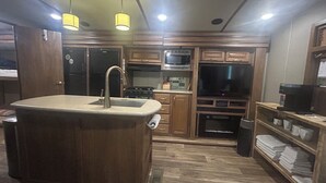 A kitchen with wooden cabinets, a central island with a sink, a microwave, stove, and a large TV. - Cozy Smoky Mtn RV with WiFi and Heat/AC near Cades Cove (Walland)