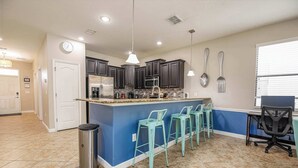 A modern kitchen with dark cabinets, a blue accent wall, a stainless steel trash can, and a bar area with bar stools. - Top Family Stay: Private Pool & Game Room (Four Corners)