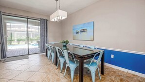 A dining area with a glass table, light blue chairs, a potted plant, and a painting of boats on the wall. - Top Family Stay: Private Pool & Game Room (Four Corners)