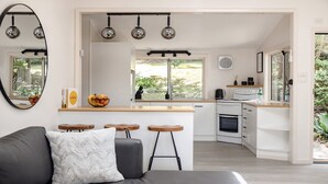 A modern kitchen with a central island, a dining area with a sofa and stools, and a large window providing a view of the outdoors.