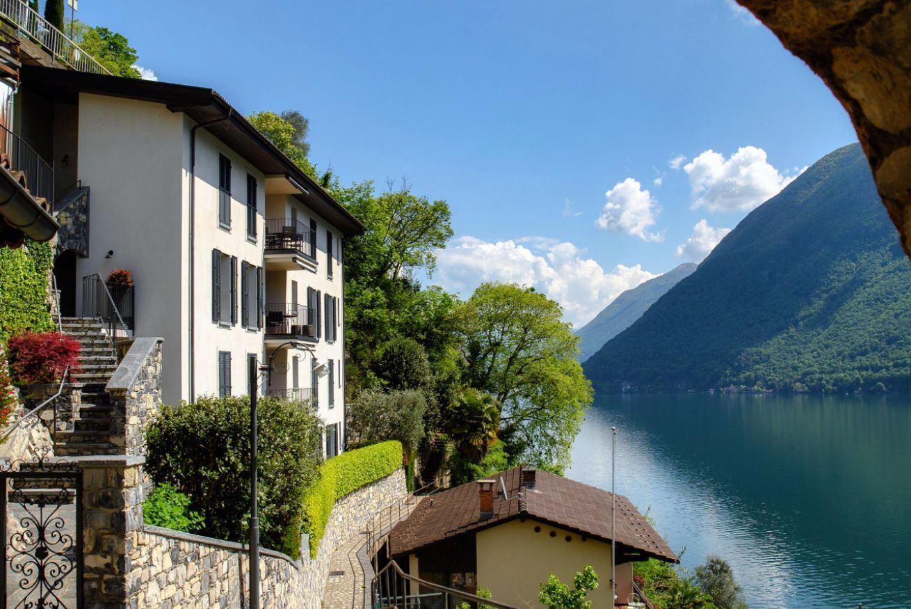 Un bâtiment à deux étages doté d’un balcon, d’un mur en pierre et offrant une vue sur un lac et des montagnes.