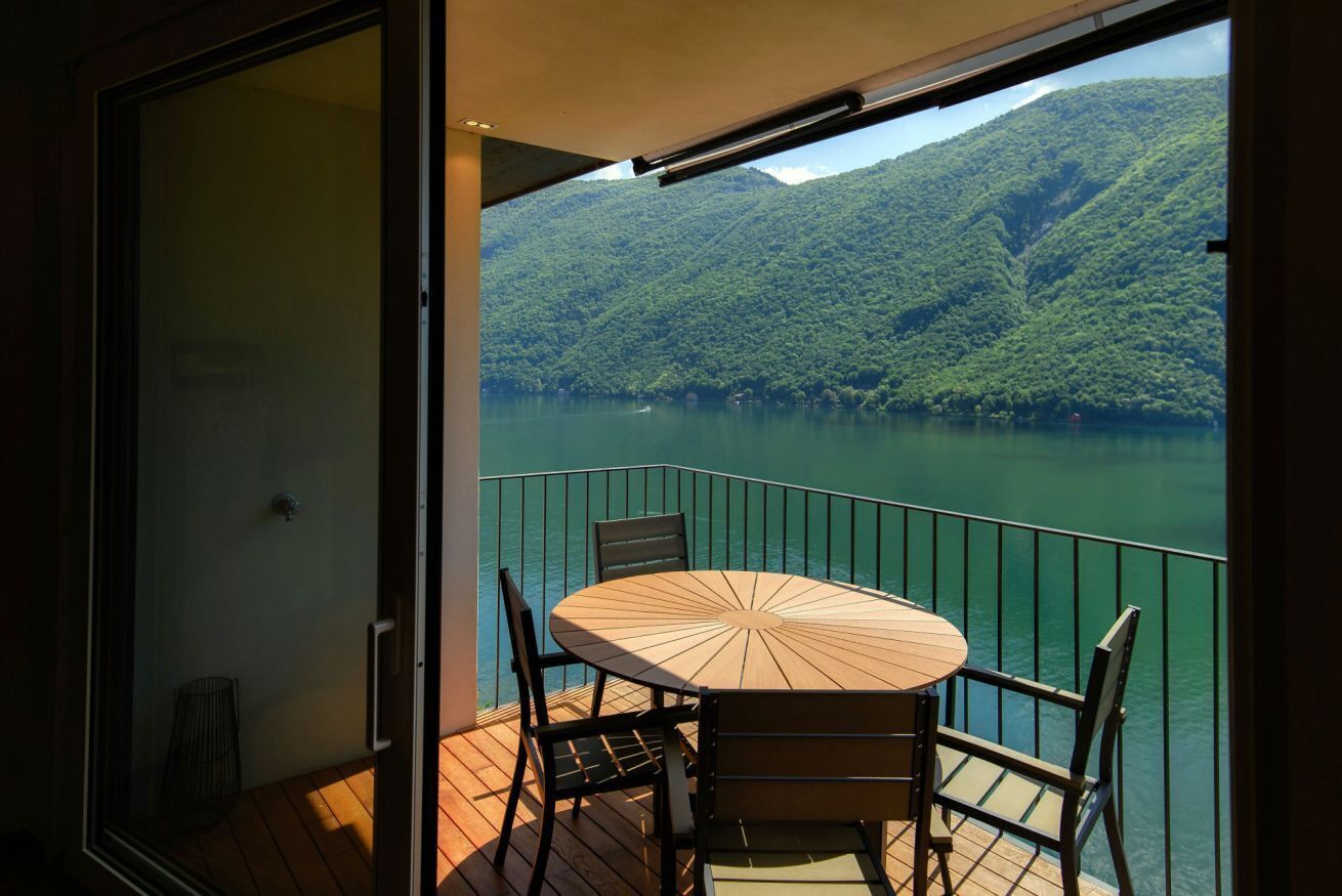 Un balcon avec une table et des chaises, donnant sur un lac et des montagnes.