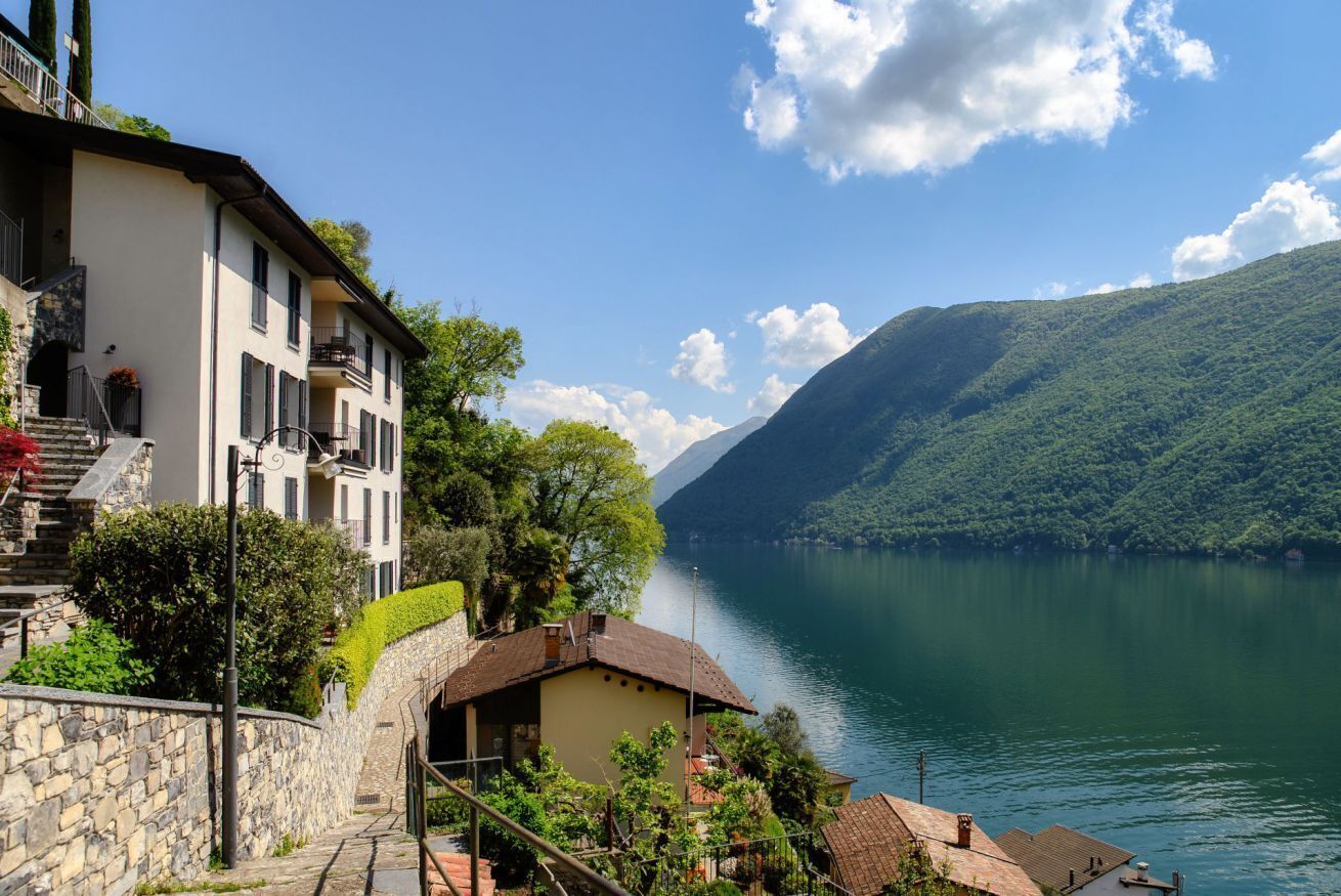 A lakeside property with a stone staircase leading to a building with multiple balconies overlooking the water.
