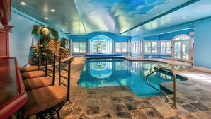 Una piscina interior con un mural en el techo, suelo de piedra y zonas de descanso.