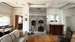 Un salón espacioso con chimenea de piedra, suelo de madera y un techo alto con molduras decorativas.