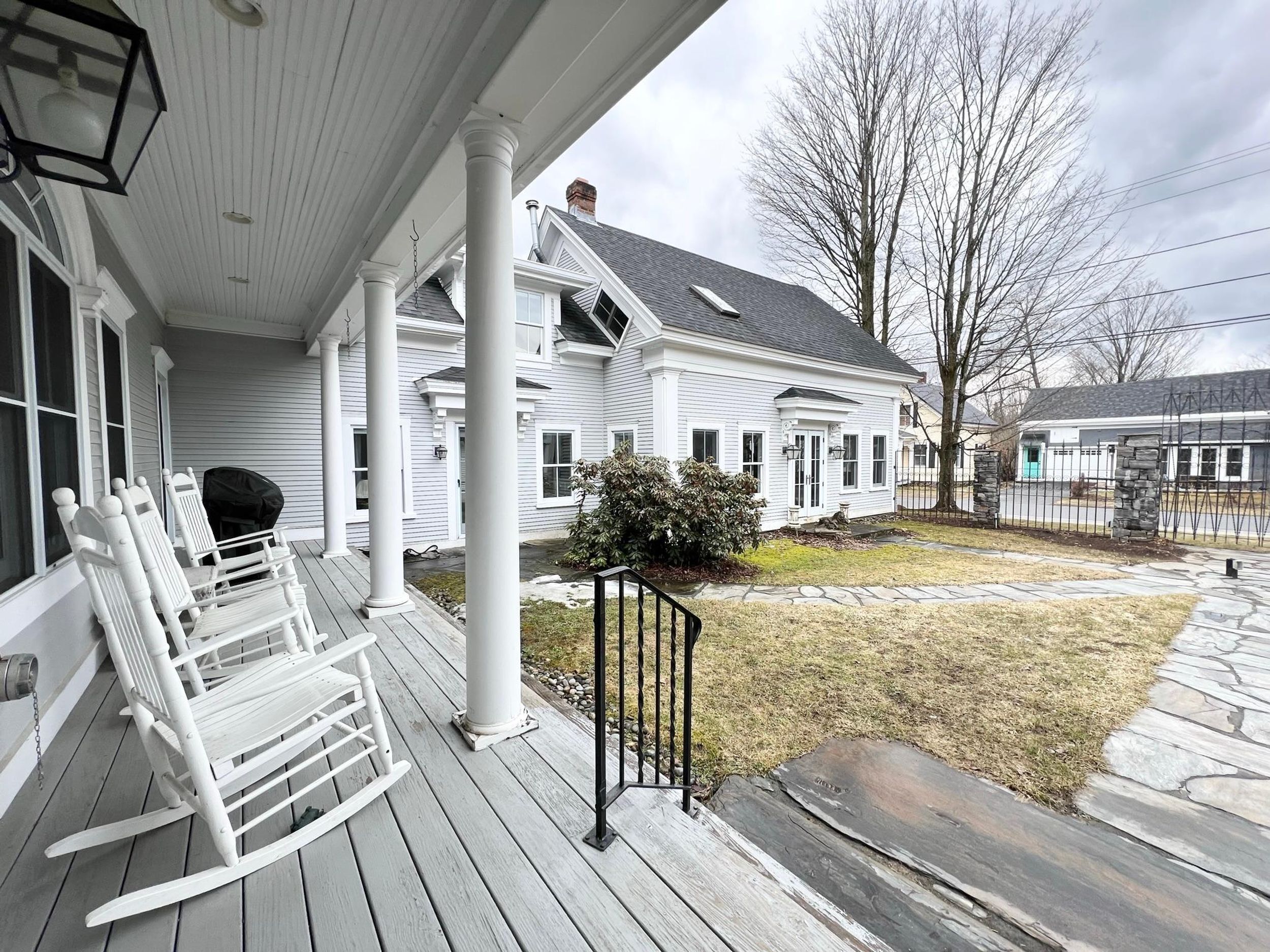 A white house with a porch, a stone pathway, and a small bush.