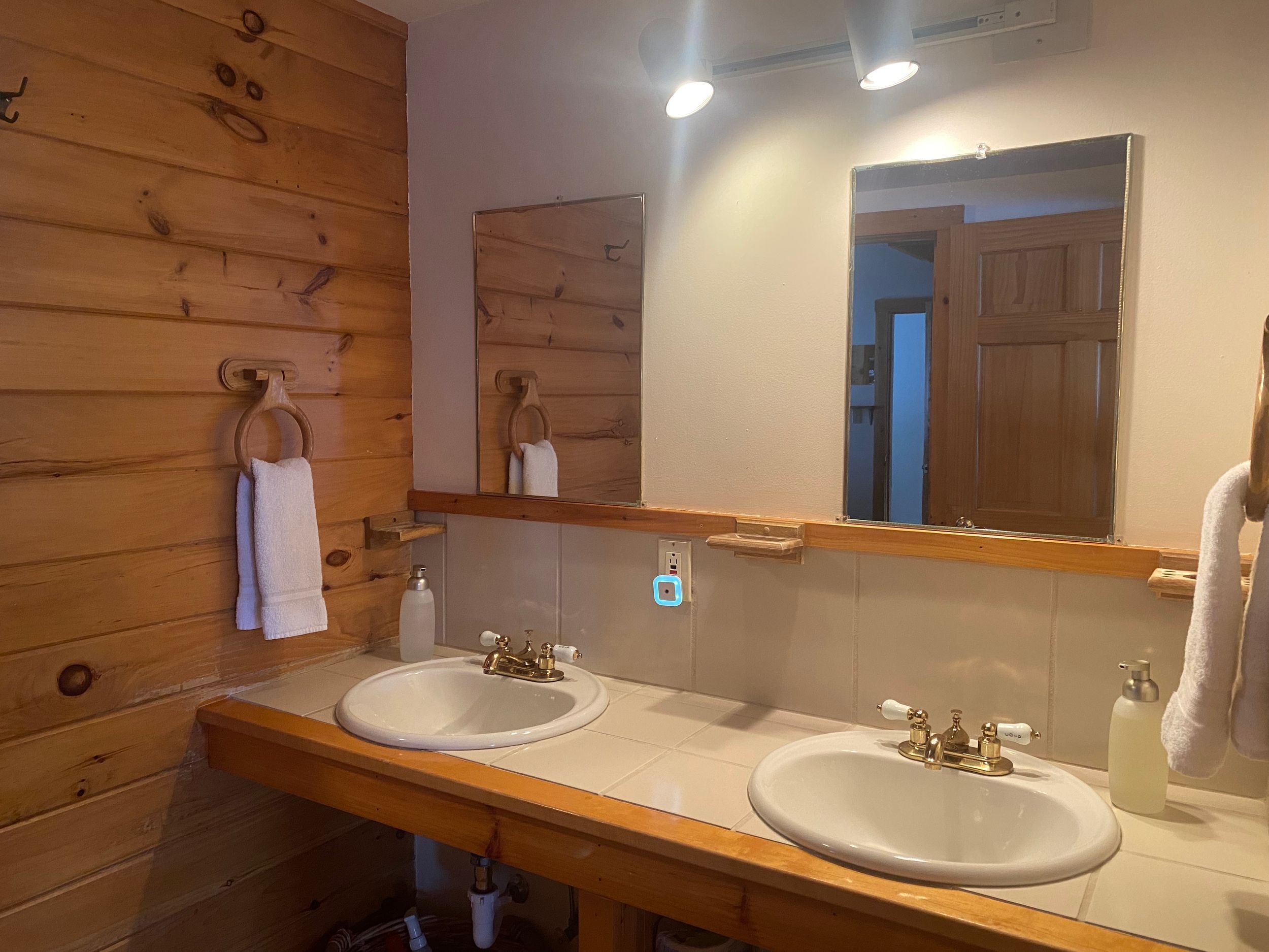 A bathroom with wooden panel walls, two sinks with faucets, a mirror, and a towel rack.